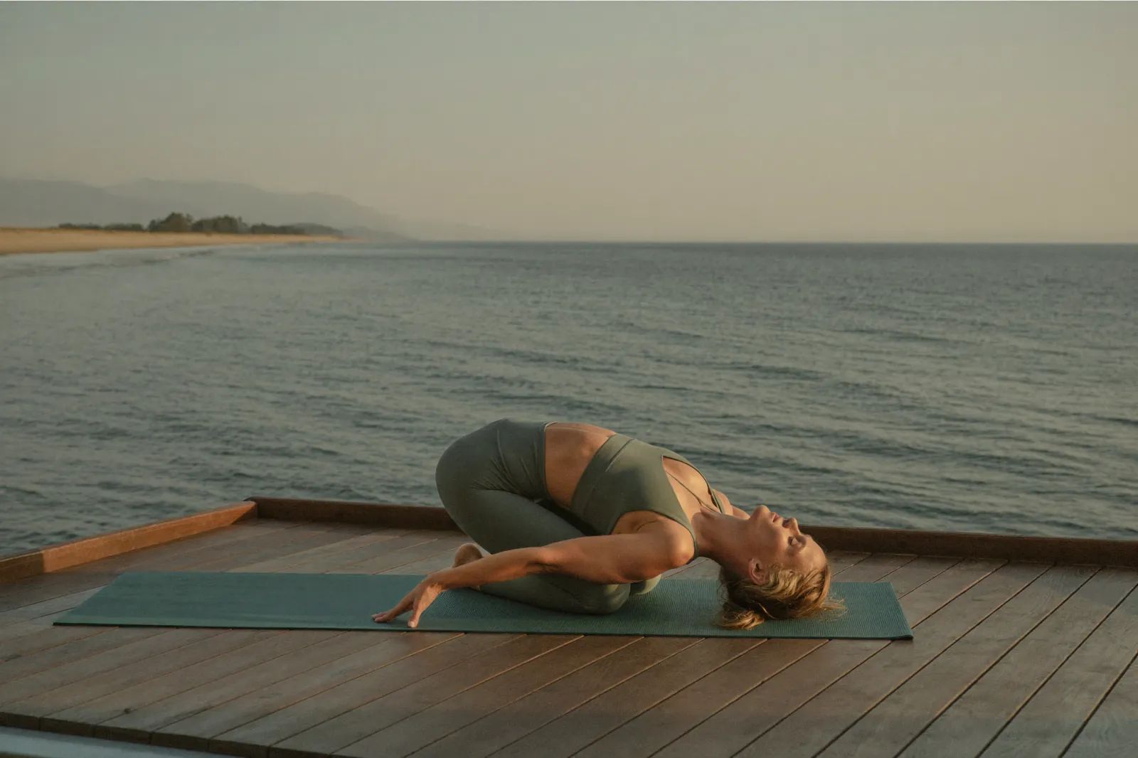 A woman stretching on a mat on a wooden deck at dawn